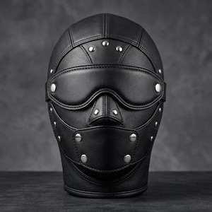 Könnte beinhalten: Eine schwarze Lederhaube mit Vollgesichtsdesign, integrierter Augenabdeckung und Mundpartie. Die Haube besteht aus mehreren vernähten Paneelen und ist mit zahlreichen silberfarbenen Metallnieten über die gesamte Außenfläche verziert.