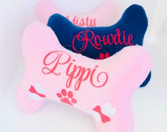 Könnte beinhalten: Drei Plüsch-Hundespielzeug in Knochenform mit gestickten Namen. Der obere Knochen ist marineblau mit dem Namen "Rowdie" in rot gestickt. Der mittlere Knochen ist rosa mit dem Namen "Misty" in rot gestickt. Der untere Knochen ist rosa mit dem Namen "Pippi" in rot gestickt.