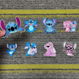 May include: A collection of nine embroidered patches featuring the character Stitch from the animated film Lilo & Stitch. The patches are in various poses and colors, primarily blue and pink, with white outlines. The patches are on a gray and yellow striped surface.