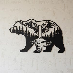 Könnte beinhalten: Schwarze Metallbären-Silhouette mit einer Berg- und Waldszene, die in ihrer Form ausgeschnitten ist. Der Bär geht nach links. Der Hintergrund ist eine hellfarbige Wand mit einem sich wiederholenden Muster aus Bäumen und Bergen.