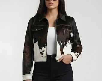 Puede incluir: Chaqueta corta de piel de vaca con un estampado marrón, negro y blanco. La chaqueta tiene un cuello clásico, dos bolsillos en el pecho y puños blancos. La modelo lleva pantalones negros y gafas de sol.