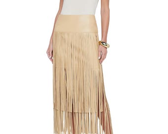 Puede incluir: Falda beige con flecos, cintura alta y aberturas laterales, combinada con una camiseta sin mangas crema. El conjunto se completa con joyas doradas y tacones beige. Los flecos de la falda añaden una textura única. La falda mide unos 90 cm de largo.