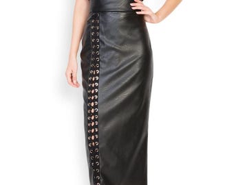 Puede incluir: Un camisón de satén negro con ribete de encaje y una falda lápiz de cuero sintético negro con un detalle de cordones. La falda tiene una cintura alta y un dobladillo a la altura de la rodilla. La modelo lleva tacones negros de punta.