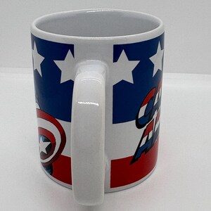 Puede incluir: Taza de cer&aacute;mica blanca con un dise&ntilde;o inspirado en el Capit&aacute;n Am&eacute;rica. La taza tiene un asa blanca y un dise&ntilde;o con colores azul, rojo y blanco. El dise&ntilde;o incluye estrellas, rayas y las palabras "Captain America".