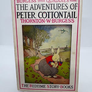 May include: Vintage hardcover book titled "The Adventures of Peter Cottontail" by Thornton W. Burgess. The cover features an illustration of a rabbit in a red jacket and checkered pants, set against a landscape with trees and a river. The book is part of "The Bedtime Story-Books" series.