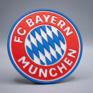 Könnte beinhalten: Ein rundes FC Bayern München Logo-Wandschild mit einem roten Außenring, weißer Schrift, einem blauen Rand und einem zentralen weißen Kreis mit einem blau-weißen Rautenmuster. Das Design ist dreidimensional mit erhabenen Elementen.