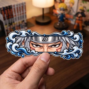 以下が含まれることがあります： とがった白い髪と渦巻きの葉のシンボルが描かれた金属製のヘッドバンドを身に着けたキャラクターのイラストが特徴の長方形のステッカー。デザインは、様式化された青い水の波と泡で縁取られています。
