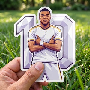 May include: A die-cut sticker featuring a cartoon illustration of a footballer wearing a white jersey with gold accents, arms crossed, positioned in front of a large, stylised number 10 with a light purple and white geometric design.