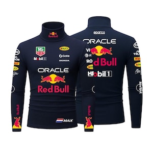 May include: Navy blue long-sleeve turtleneck shirt featuring multiple logos, including "Red Bull" and "Oracle." The shirt has a high collar and is adorned with various sponsor logos. The design includes red and yellow accents.