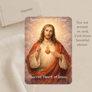Op de afbeelding: Een religieuze kaart met een afbeelding van Jezus met een stralend hart en een gouden halo. De kaart heeft de tekst "Heilig Hart van Jezus" bovenaan en onderaan. Een planner is zichtbaar op de achtergrond.