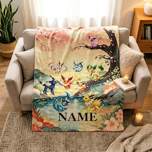 May include: A soft throw blanket featuring a colorful illustration of various Eevee evolution characters in a landscape with a tree, a pond, and cherry blossoms. The word NAME is printed in black serif font at the bottom center of the blanket.