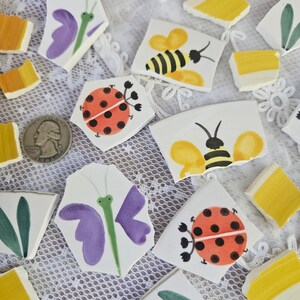 May include: Hand-painted ceramic tiles featuring insect designs. The tiles include a ladybug, bee, and butterfly, with a quarter coin for size reference. The tiles are white with colorful accents of red, yellow, green, and purple.