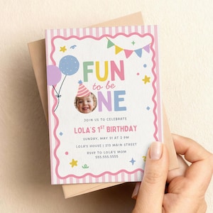 Op de afbeelding: Een rechthoekige verjaardagsuitnodigingskaart met een roze en wit gestreepte rand en een geschulpte roze omlijsting. De tekst luidt FUN to be ONE, JOIN US TO CELEBRATE, LOLA'S 1ST BIRTHDAY, SUNDAY, MAY 31 AT 2 PM, LOLA'S HOUSE, 213 MAIN STREET, RSVP TO LOLA'S MOM 555.555.5555.