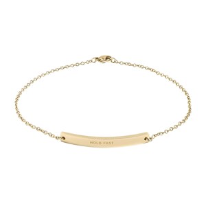Può includere: Un delicato braccialetto color oro con un design a catena. Il braccialetto presenta un pendente curvo con le parole "HOLD FAST" incise. Il gioiello è progettato per l'uso quotidiano.