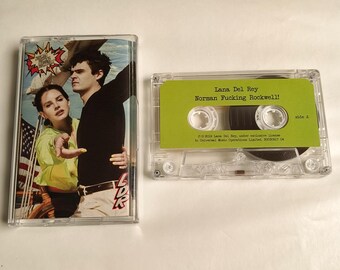Puede incluir: Dos cintas de cassette. Una tiene una portada con una foto de un hombre y una mujer, y el texto "Lana Del Rey". La otra cinta tiene una etiqueta verde con el texto "Lana Del Rey Norman Fucking Rockwell!"