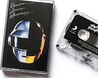 May include: A clear cassette tape and case featuring the album "Random Access Memories" by Daft Punk. The case has a black background with a silver and gold helmet design. The cassette tape is black with white text.