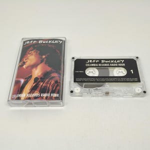 Peut inclure: Une cassette et son boîtier transparents avec l'album "Jeff Buckley Columbia Records Radio Hour". Le boîtier affiche une photo de Jeff Buckley chantant dans un microphone. La cassette porte le titre de l'album et le chiffre "1".