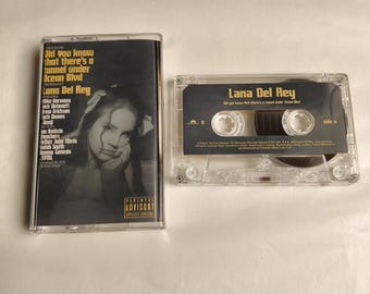 May include: Two clear cassette tapes. One has a black and white image of a woman and the text "Did You Know That There's A Tunnel Under Ocean Blvd" by Lana Del Rey. The other tape is visible with the same text.