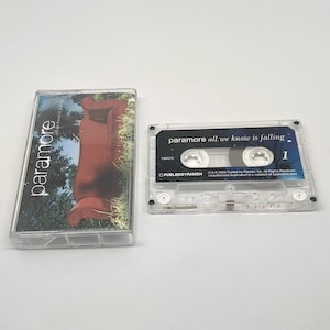 May include: A clear cassette tape and case featuring the band Paramore. The cassette case has a cover image with the band's name and a blurred image of a person. The cassette tape is labeled "paramore all we know is falling."