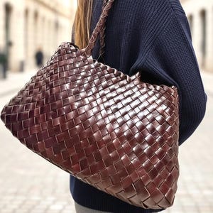Peut inclure: Un sac fourre-tout marron foncé doté d'un motif tressé complexe sur tout le corps et de deux bandoulières tressées. Le sac est fabriqué à partir de larges bandes entrelacées avec une finition lisse et brillante d'un ton marron foncé uniforme.