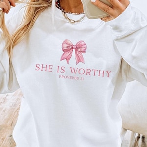 May include: White sweatshirt with a pink bow and the text "SHE IS WORTHY PROVERBS 31" printed on the front.