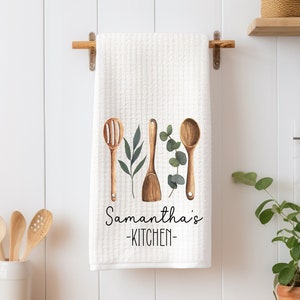 May include: White kitchen towel with a watercolor design of wooden kitchen utensils and green leaves. The text "Samantha's -KITCHEN- " is printed on the towel.
