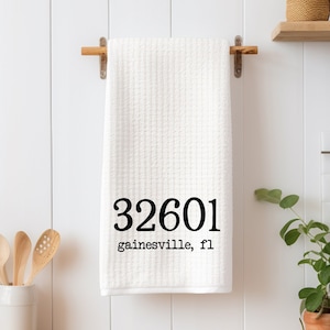 May include: White kitchen towel with black text that reads "32601 Gainesville, FL".