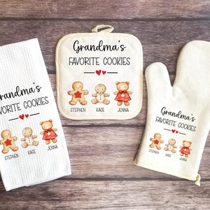 May include: Set of three kitchen textiles featuring a gingerbread cookie design with the text "Grandma's Favorite Cookies". The set includes a tea towel, a pot holder, and an oven mitt. Each item features three gingerbread cookies with the names "Stephen", "Kace", and "Jenna" printed below.