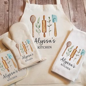 May include: A set of four kitchen towels with a watercolor design of kitchen utensils and the text "Alyssa's Kitchen". The towels are white with a light brown background.