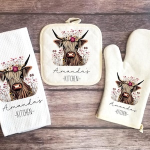 May include: A set of three kitchen towels featuring a Highland cow with floral accents. The towels are white with black text that reads "Amanda's Kitchen".