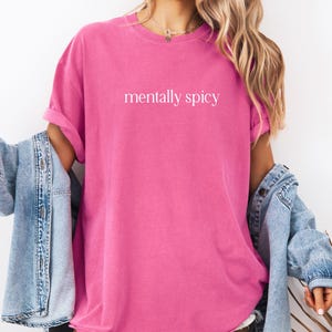 May include: A pink t-shirt with the text "mentally spicy" printed in white on the front.