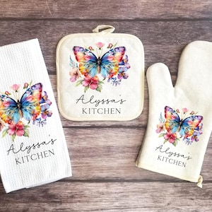 May include: A white kitchen towel, pot holder, and oven mitt set. Each item features a watercolor butterfly design with pink, blue, and yellow hues, surrounded by flowers. The text "Alyssa's KITCHEN" is printed on each item.