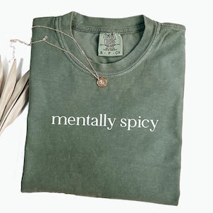 May include: A green t-shirt with the text "mentally spicy" printed in white on the front. The shirt is made of a soft, comfortable material and has a relaxed fit.