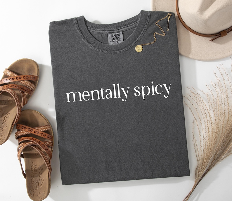 May include: A dark grey t-shirt with the text "mentally spicy" printed in white on the front.