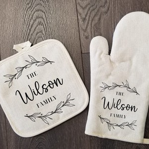 May include: A set of two white cotton oven mitts with black floral designs and the text "The Wilson Family".