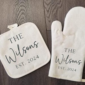 May include: A set of two white cotton oven mitts with black text that reads "THE Wilsons EST. 2024".