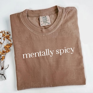 May include: A brown t-shirt with the text "mentally spicy" printed in white on the front. The shirt is made of a soft, comfortable fabric and has a relaxed fit.