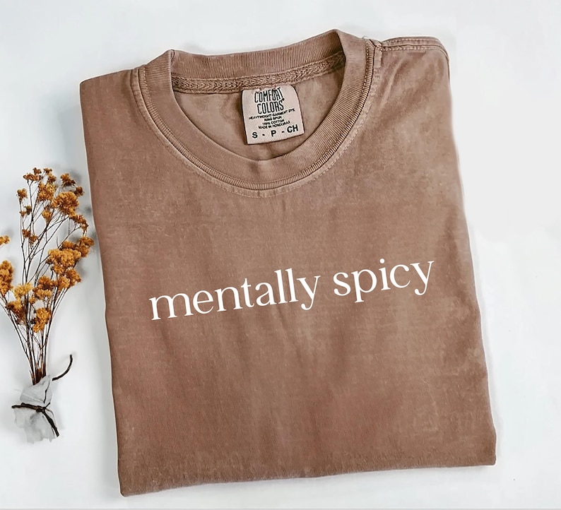 May include: A brown t-shirt with the text "mentally spicy" printed in white on the front. The shirt is made of a soft, comfortable fabric and has a relaxed fit.