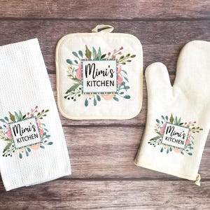May include: A set of three kitchen items with a floral design and the text "Mimi's Kitchen". The set includes a tea towel, a pot holder, and an oven mitt.