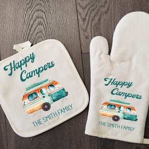 May include: A set of two kitchen textiles featuring a vintage camper van design. The pot holder and oven mitt are both white with green and orange accents. The text "Happy Campers" and "The Smith Family" is printed on both items.