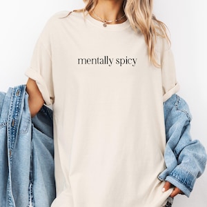 May include: A beige t-shirt with the text "mentally spicy" printed in black.