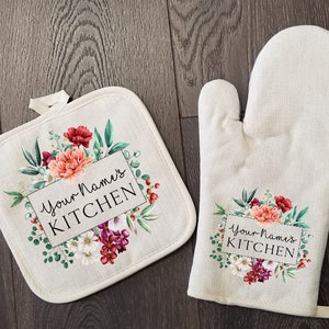 May include: A set of two kitchen pot holders with a floral design and the text "Your Name's Kitchen".