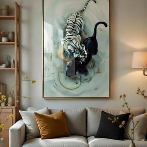 Puede incluir: Una impresión artística enmarcada que presenta un tigre blanco y una pantera negra en un entorno acuático. La obra de arte tiene un marco dorado y cuelga sobre un sofá gris claro con cojines decorativos. La habitación tiene una paleta de colores neutros.