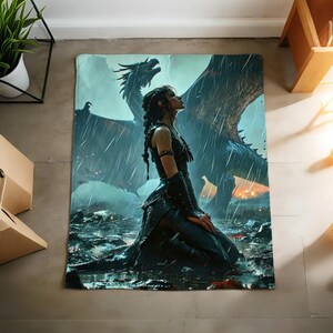 K&ouml;nnte beinhalten: Eine Fantasy-Decke mit einer knienden Frau im Regen und einem Drachen im Hintergrund. Die Kunst verwendet Blau-, Grau- und Schwarzt&ouml;ne, wodurch eine dramatische Szene entsteht. Die Decke ist rechteckig und f&uuml;r Betten oder Sofas geeignet.