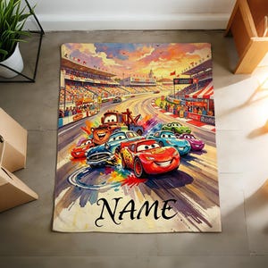 Pu&ograve; includere: Una coperta rettangolare con una colorata illustrazione di auto da corsa animate su una pista con uno stadio sullo sfondo. Il design include un'auto rossa con il numero 95, un'auto blu e un carro attrezzi marrone. La parola NAME &egrave; stampata in nero.