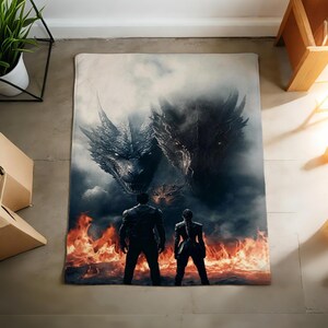 K&ouml;nnte beinhalten: Eine rechteckige Decke mit einer Fantasy-Szene mit zwei Drachen und zwei Figuren, die vor einer feurigen Landschaft stehen. Die Drachen sind mit dunkelgrauen Schuppen detailliert, und die Figuren tragen schwarze Kleidung.