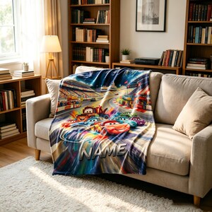 Pu&ograve; includere: Una morbida coperta in pile con una vivace e colorata scena di pista da corsa con diverse auto da corsa animate antropomorfe in movimento. Il design include la parola NAME in lettere metalliche nella parte inferiore della coperta.