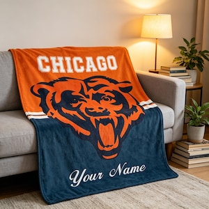 May include: A plush throw blanket featuring the word CHICAGO in white block letters above a large orange and navy blue bear head graphic. The lower section is navy blue with the white script text Your Name centered below the bear illustration.