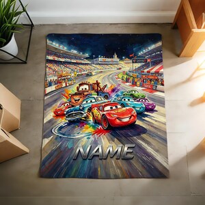 Pu&ograve; includere: Un tappeto rettangolare con un'illustrazione artistica e colorata di varie auto da corsa del film Cars, tra cui Saetta McQueen e Cricchetto, su un circuito con tribune. La parola NAME &egrave; stampata in grandi lettere color argento.
