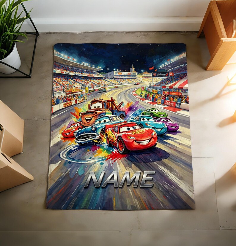Pu&ograve; includere: Un tappeto rettangolare con un'illustrazione artistica e colorata di varie auto da corsa del film Cars, tra cui Saetta McQueen e Cricchetto, su un circuito con tribune. La parola NAME &egrave; stampata in grandi lettere color argento.